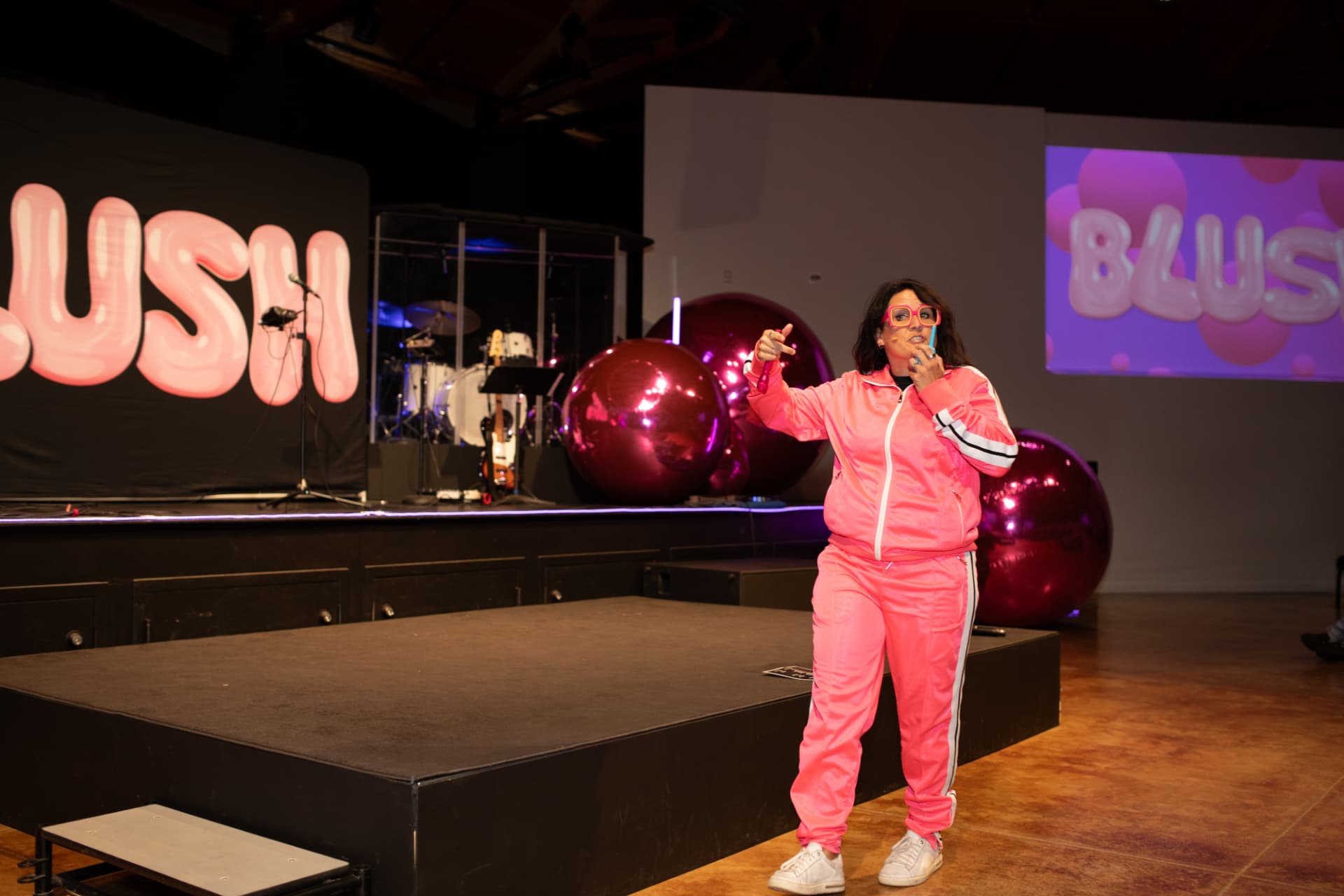 Speaker on stage at BLUSH in a pink tracksuit pointing to the crowd